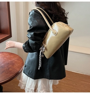 Détail du sac Boston beige avec pendentif cœur et bandoulière tissée porté par un mannequin