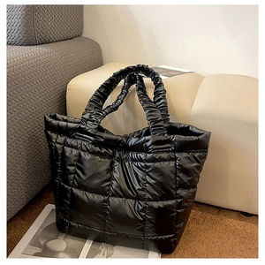 Detail of black quilted down tote bag featuring puffer texture and pleated handles