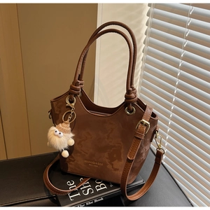 Detail of dark brown tote bag with logo, detachable strap and plush doll pendant