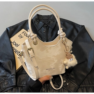 Detail of cream tote bag with marble texture, knotted handle, and plush monster charm