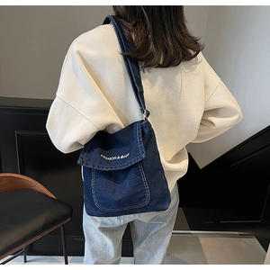 Vista posteriore della modella con borsa a tracolla in denim blu con scritte bianche