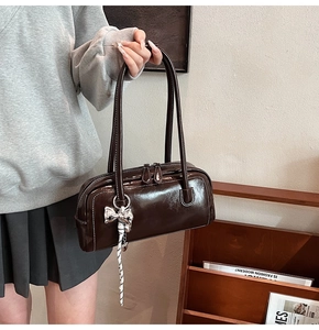 Détail du sac Boston marron foncé brillant avec pendentif nœud argenté et double zip
