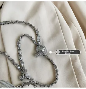 Détail macro de la bandoulière chaîne argentée avec boule matelassée sur tissu beige