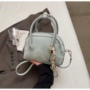 Detail of mint green matte leather boston bag with vintage key charm and woven cord