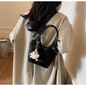 Close-up of black oil wax leather bucket bag with gold logo and plush doll pendant