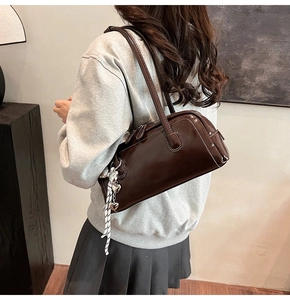 Détail du sac Boston marron brillant avec breloque cœur porté à l'épaule par un mannequin