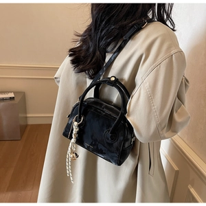 Detail of a black glossy Boston bag featuring a stylish woven knot charm on a trench coat model