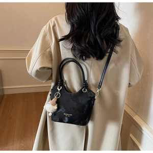 Detail of black faux leather tote bag with white plush charm on a model in a trench coat