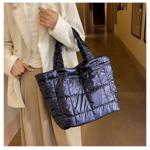 Close-up of metallic blue quilted puffer tote bag with ruched handles on a model