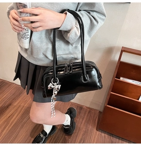 Détail du sac Boston noir brillant avec pendentif nœud argenté et fermeture éclair