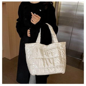 Close-up of a white quilted puffer tote bag with metallic finish and wide handles