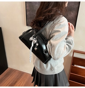 Détail du sac Boston en cuir verni noir avec nœud argenté et breloques cœur sur la bandoulière