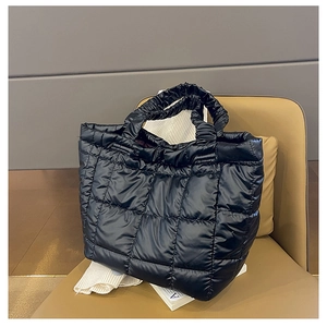 Detail of black quilted puffer tote bag with glossy nylon texture on a leather seat