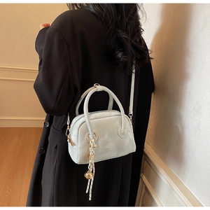 Detail of glossy patent leather handbag with decorative knot and gold ball charm