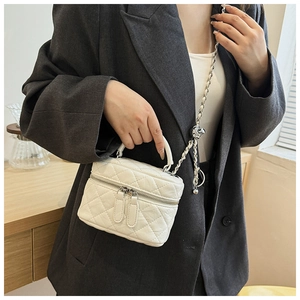 Détail du sac bandoulière matelassé blanc avec chaîne en métal et poignée sur un blazer