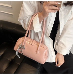 Gros plan du sac Boston en cuir verni rose avec breloque nœud argenté et pendentif tissé