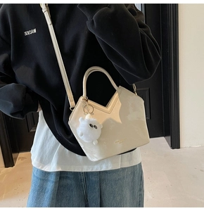 Détail du sac seau en cuir verni crème avec ouverture en V et breloque ours en peluche