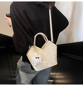Détail du sac seau crème avec ouverture en V et breloque en peluche sur un mannequin