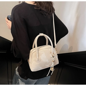 Detail of minimalist cream leather handbag featuring woven cord charm and golden orb detail