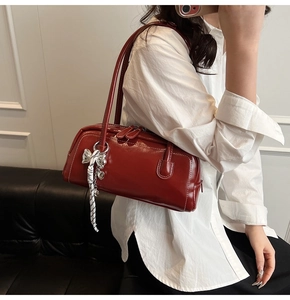 Détail du sac Boston en cuir verni bordeaux avec charm nœud argenté et ruban