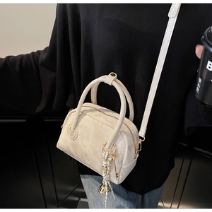 Close-up of a cream Boston handbag with a decorative knot charm and metallic sphere