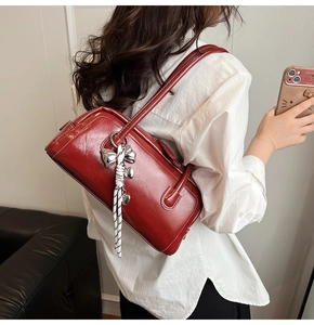 Gros plan d'un sac bandoulière en cuir brillant bordeaux avec breloque nœud argenté