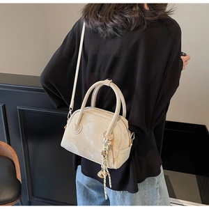 Detail of cream Boston bag with glossy leather texture, woven knot and golden ball charm