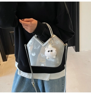 Détail d'un sac seau en cuir verni argenté avec un pendentif en peluche et logo