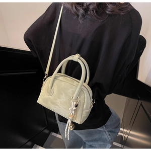 Detailed side view of mint green leather Boston handbag with woven cord and metal charm