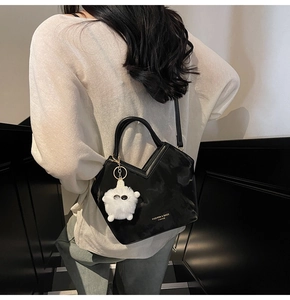 Détail du sac seau noir brillant avec ouverture en V et charm en peluche blanche sur modèle