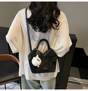 Détail du sac seau noir en cuir brillant avec coupe en V et charm pompon blanc en peluche