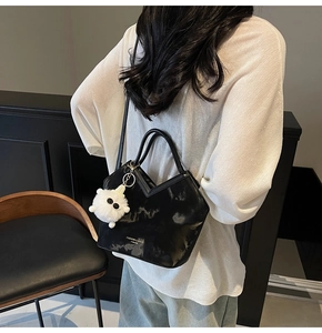 Détail du sac cabas en cuir brillant noir avec ouverture en V et breloque peluche