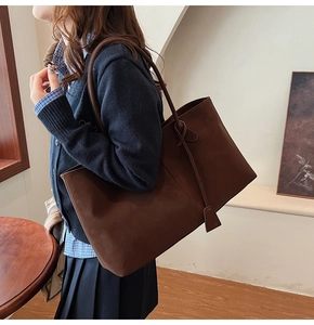 Detail view of large dark brown suede tote bag worn on shoulder in a retro interior setting