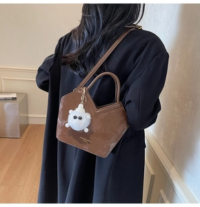 Détail du sac seau marron brillant avec ouverture en V et breloque en forme d'ours peluche