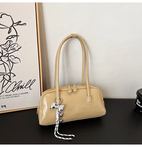 Gros plan d'un sac à main en cuir verni beige avec double zip et pendentif nœud argenté