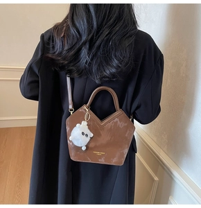 Détail d'un sac seau marron brillant avec coupe en V et un petit pendentif mouton en peluche