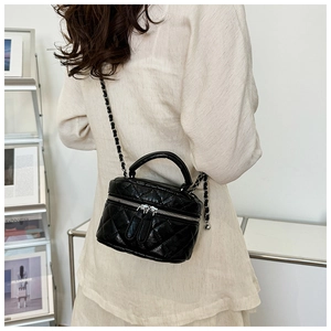 Détail d'un mini sac seau matelassé noir avec chaîne argentée porté par un modèle