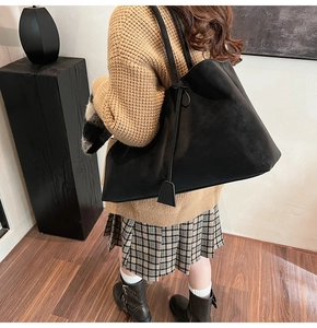 Close-up of black matte suede tote bag with minimalist shoulder strap and tag details