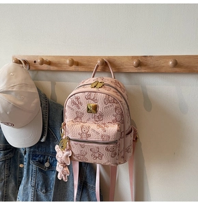 Roze mini rugzak met teddybeer print en gouden logo hangend aan een houten haak