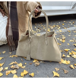 Detail of khaki suede tote bag with slim handles and tag against autumn ginkgo leaves