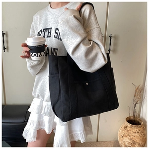 Detail of black canvas tote bag with snap button front pocket and side storage pockets