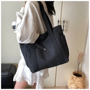 Detail view of black canvas tote bag with snap-button front pocket and side storage