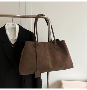 Close-up of deep brown matte suede tote bag with long handles hanging in a wardrobe