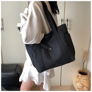 Side view of large black canvas tote bag with side pockets and front snap pocket