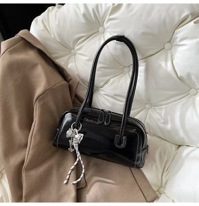 Détail du sac Boston noir brillant avec surpiqûres blanches et breloque nœud argenté