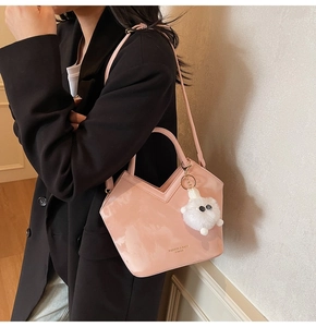 Détail du sac seau rose en cuir verni brillant avec charme en peluche sur blazer noir