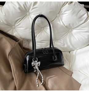 Détail du sac Boston noir avec surpiqûres blanches et pendentif nœud argenté élégant