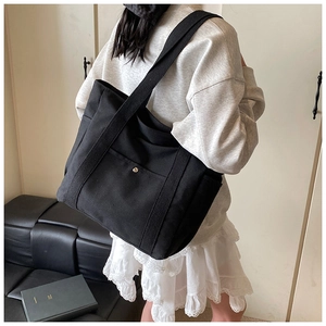 Schwarze Canvas-Einkaufstasche mit Vordertasche und goldener Schnalle am Modell