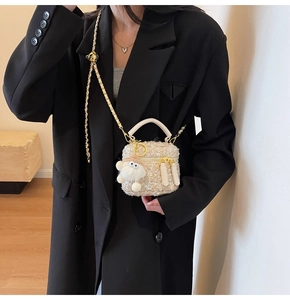 Detail of beige tweed mini crossbody bag with gold chain and plush charm on black blazer