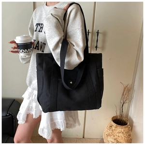 Detail view of a large black canvas tote bag with front snap pocket on a model